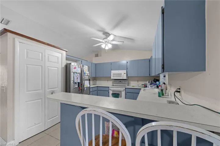 Kitchen with blue cabinets, lofted ceiling, white appliances, light countertops, and a peninsula