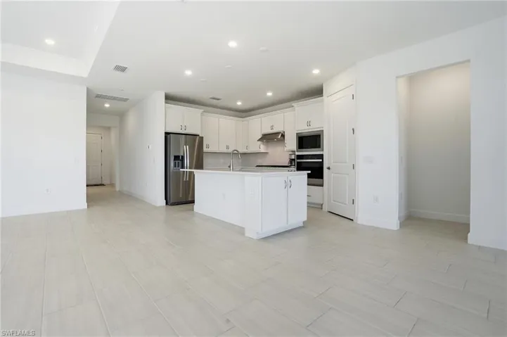 Kitchen with white cabinetry, stainless steel appliances, an island with sink, light countertops, and open floor plan