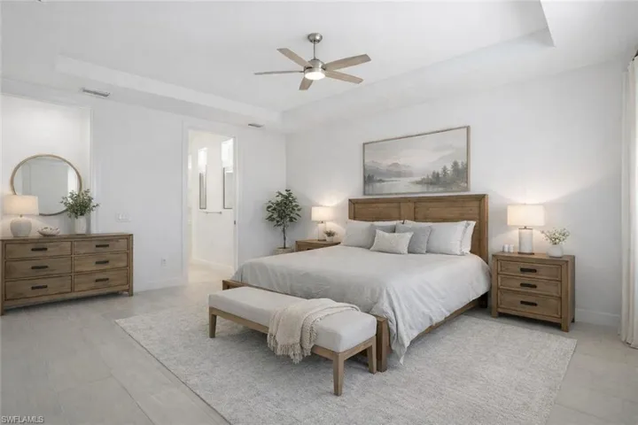 Virtually staged- Bedroom featuring a tray ceiling, ceiling fan, and ensuite bath