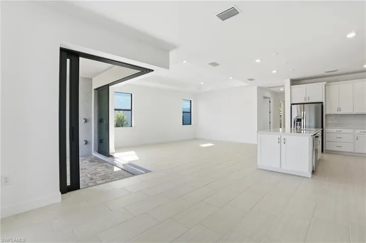 Kitchen featuring white cabinetry, open floor plan, an island with sink, stainless steel refrigerator with ice dispenser, and decorative backsplash