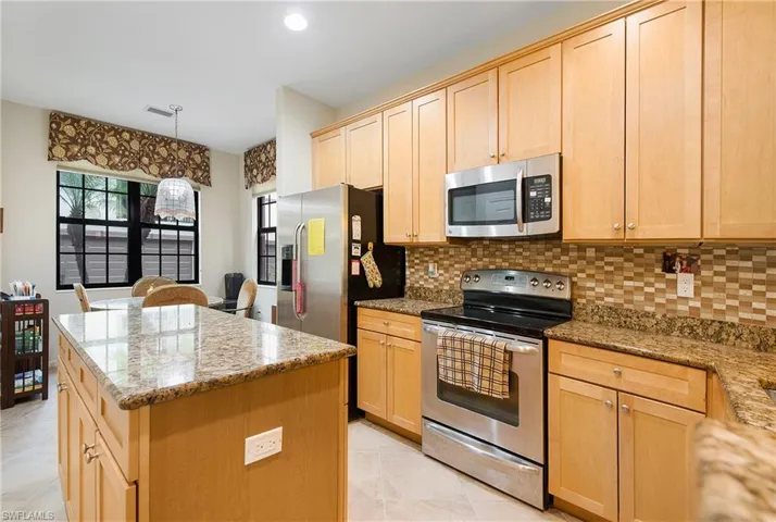 Kitchen featuring stainless steel appliances, light brown cabinetry, a center island, backsplash, and light stone countertops