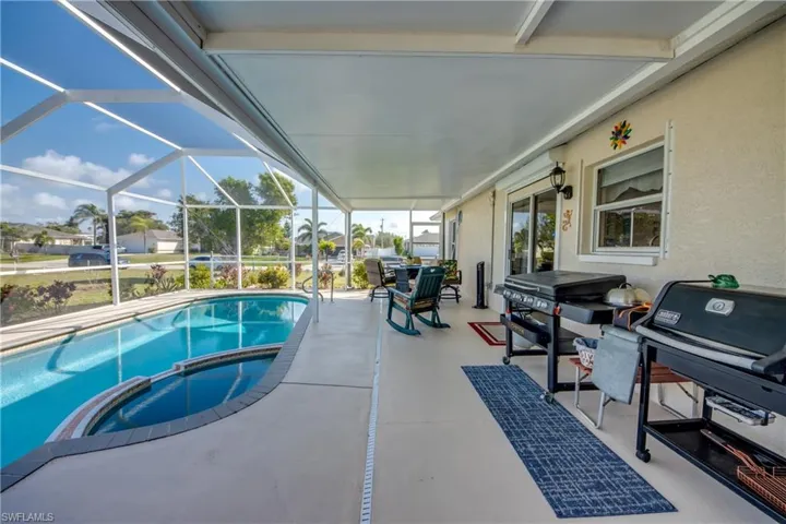 View of pool with a patio area, grilling area, glass enclosure, and an in ground hot tub