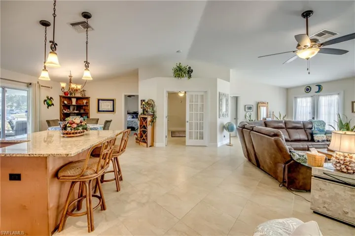 Kitchen featuring vaulted ceiling, a breakfast bar area, hanging light fixtures, ceiling fan, and light stone counters