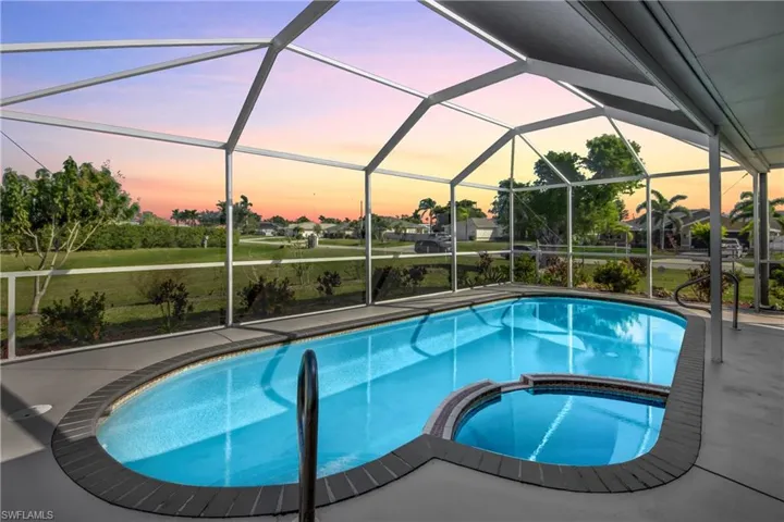 Pool at dusk with an in ground hot tub, a patio area, and glass enclosure