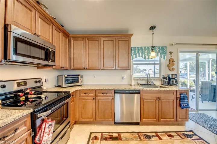 Kitchen featuring pendant lighting, sink, light tile patterned floors, stainless steel appliances, and light stone countertops