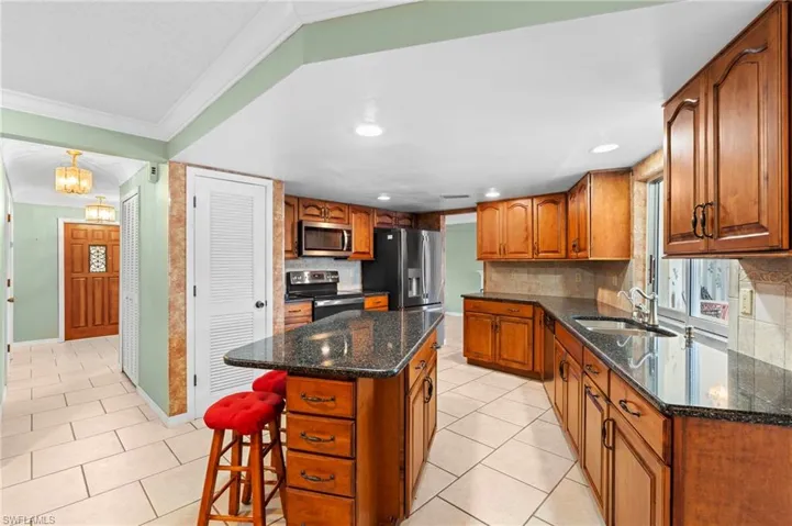 Kitchen featuring appliances with stainless steel finishes, brown cabinets, a sink, light tile patterned flooring, and ornamental molding