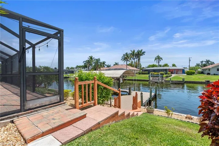 Dock area featuring a water view, a lawn, glass enclosure, and boat lift  Photo virtually enhanced.