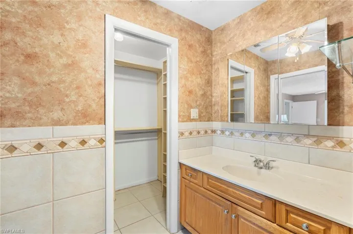 Bathroom with ceiling fan, tile walls, a walk in closet, tile patterned floors, and vanity