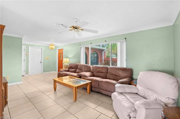 Living room featuring a ceiling fan, light tile patterned floors, and a textured ceiling