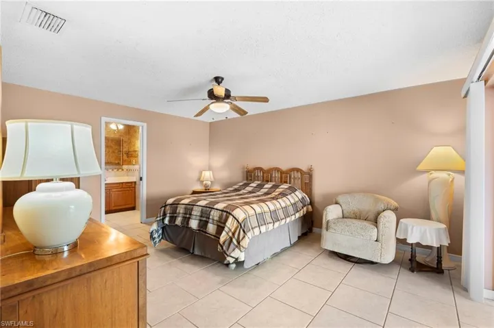 Bedroom with light tile patterned floors, a textured ceiling, ceiling fan, baseboards, and connected bathroom