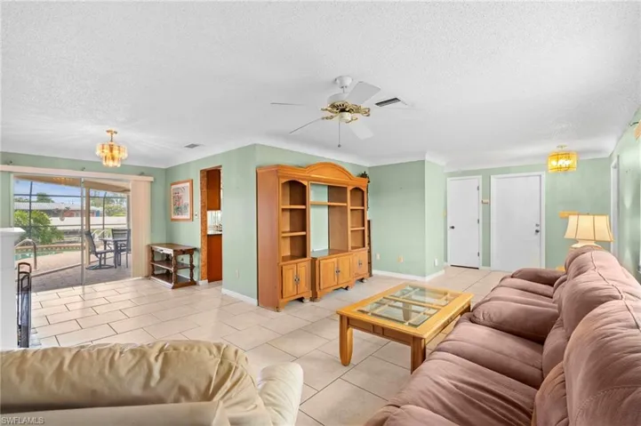 Living area featuring a textured ceiling, a chandelier, light tile patterned floors, a ceiling fan, and baseboards
