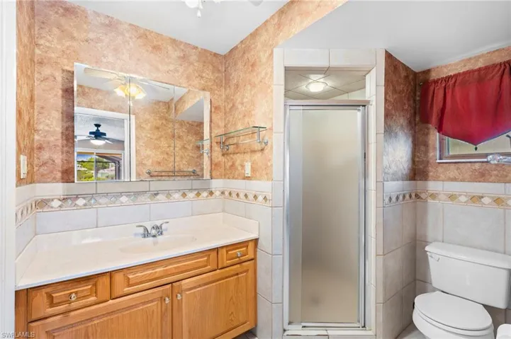Bathroom featuring tile walls, a ceiling fan, a stall shower, toilet, and vanity