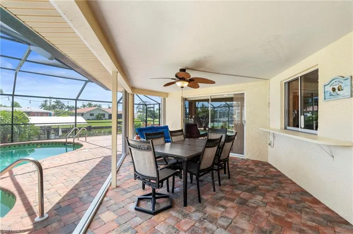 View of patio / terrace with a ceiling fan, a lanai, an outdoor pool, and outdoor dining space  Photo virtually enhanced.