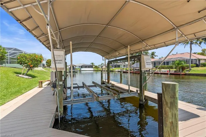 Dock area with boat lift, a water view, a yard, and a residential view  Photo virtually enhanced.
