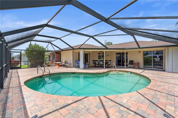 Outdoor pool with a patio, outdoor dining space, glass enclosure, and a ceiling fan  Photo virtually enhanced.