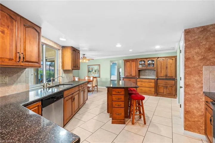 Kitchen featuring stainless steel dishwasher, a sink, baseboards, brown cabinetry, and a kitchen bar