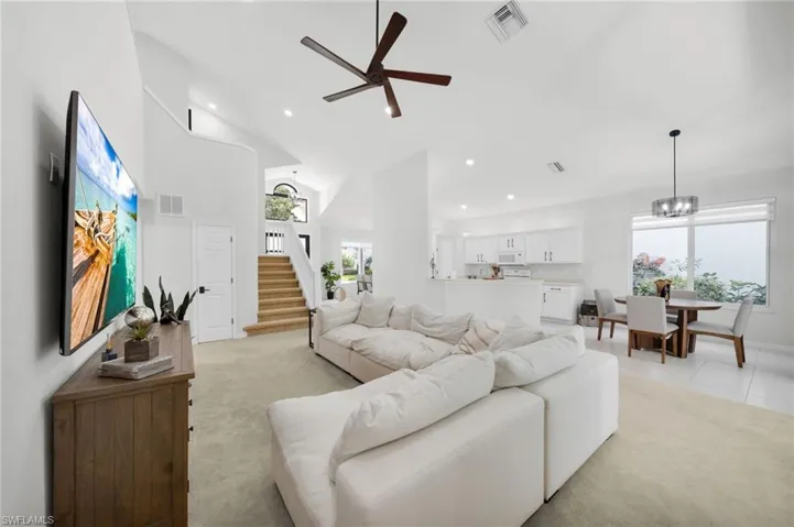 Living room with ceiling fan, light carpet, hanging lights, and lofted ceiling