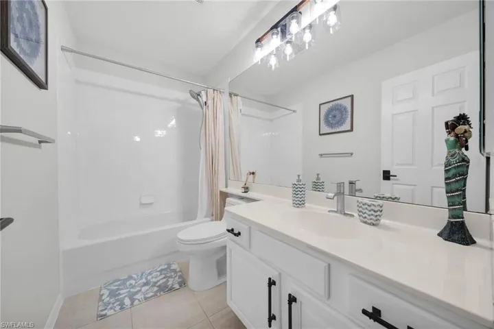 Full bathroom with vanity, shower / bath combo with shower curtain, and light tile patterned floors