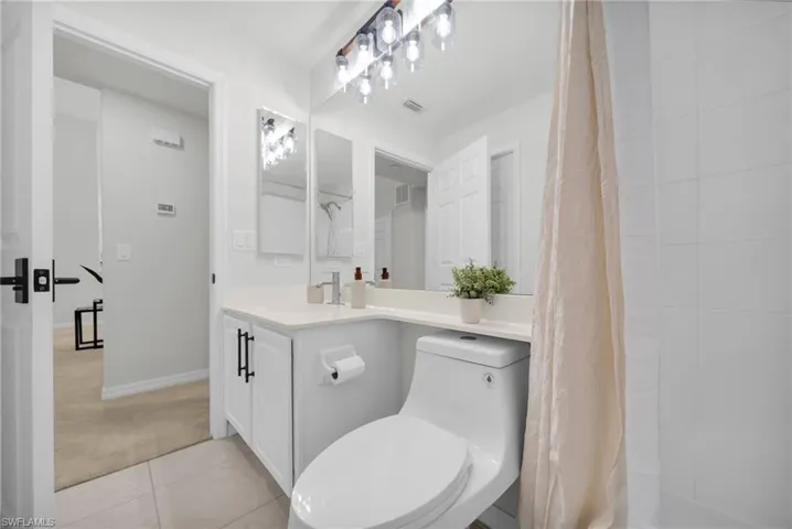 Bathroom with tiled shower, vanity, light colored carpet, and light tile patterned flooring