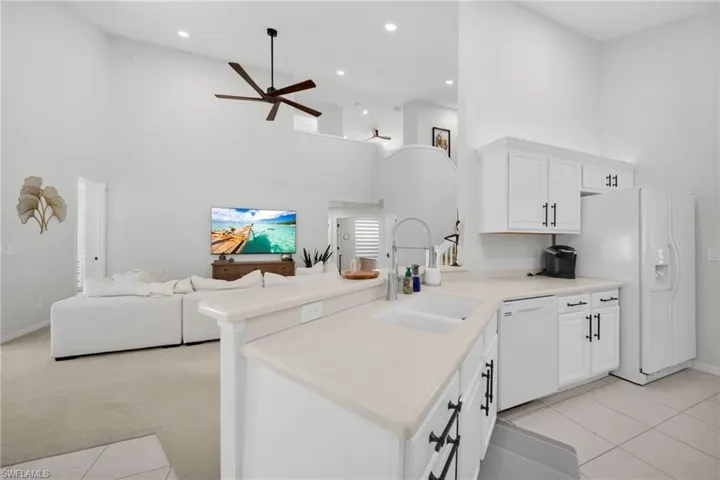 Kitchen featuring a peninsula, a high ceiling, white cabinets, white appliances, and light countertops