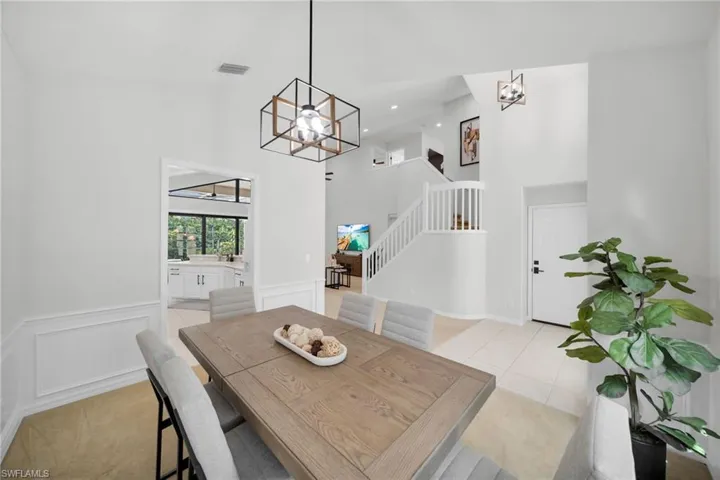 Dining area with suspended lighting, a high ceiling, a wainscoted wall, light tile patterned floors, and a decorative wall