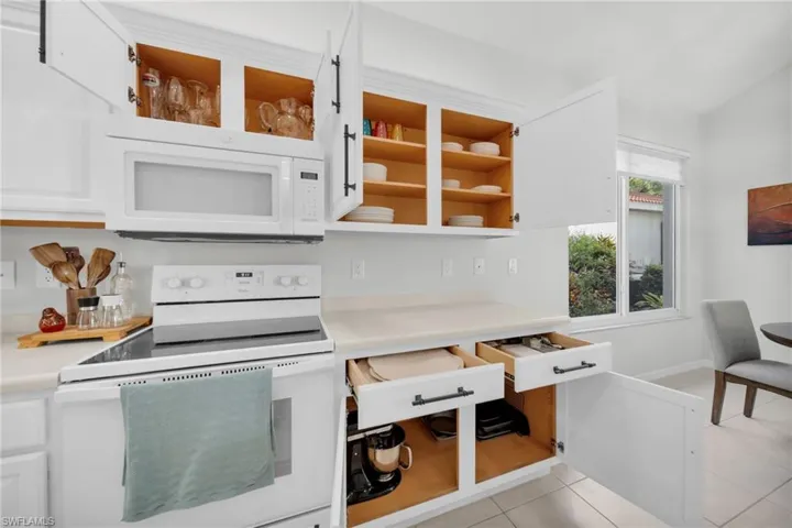 Kitchen featuring white appliances, light countertops, white cabinets, light tile patterned flooring, and open shelves