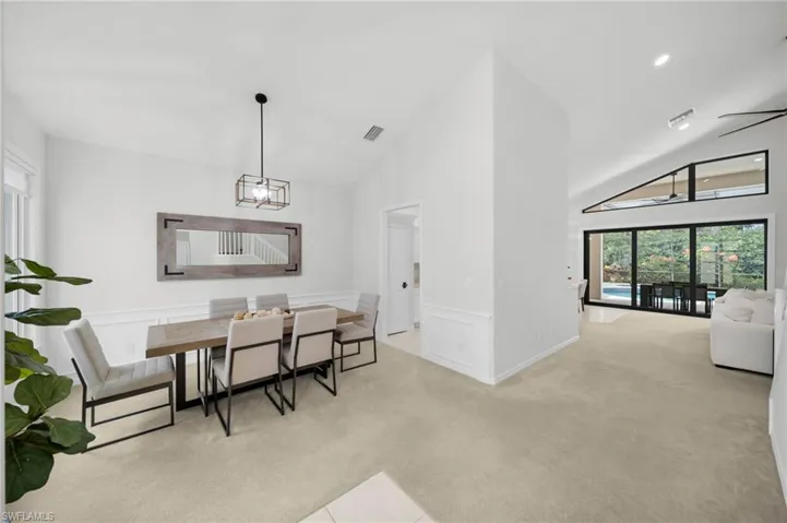 Dining room featuring healthy amount of natural light, light carpet, vaulted ceiling, a decorative wall, and wainscoting