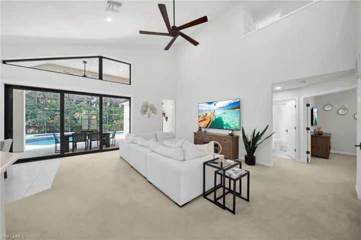 Living room with ceiling fan, light colored carpet, recessed lighting, and a high ceiling