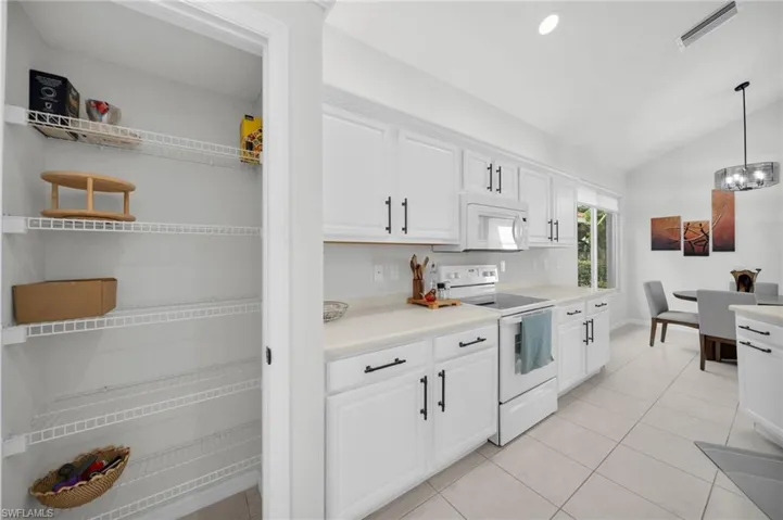 Kitchen featuring white appliances, lofted ceiling, white cabinets, and light countertops