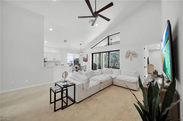 Living room with light colored carpet, a ceiling fan, recessed lighting, and lofted ceiling