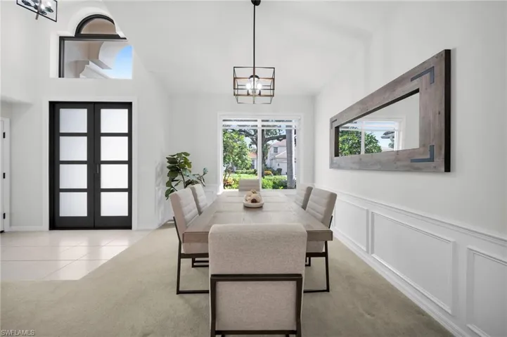Dining area featuring suspended lighting, french doors, wainscoting, a decorative wall, and light colored carpet