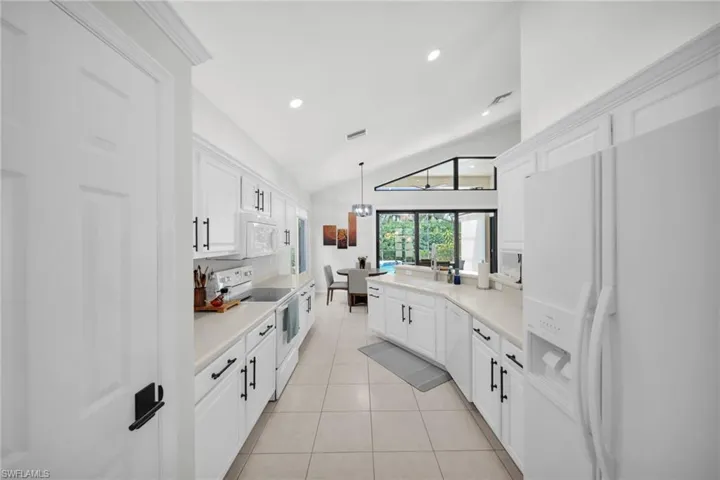 Kitchen featuring white appliances, vaulted ceiling, light countertops, light tile patterned floors, and white cabinetry