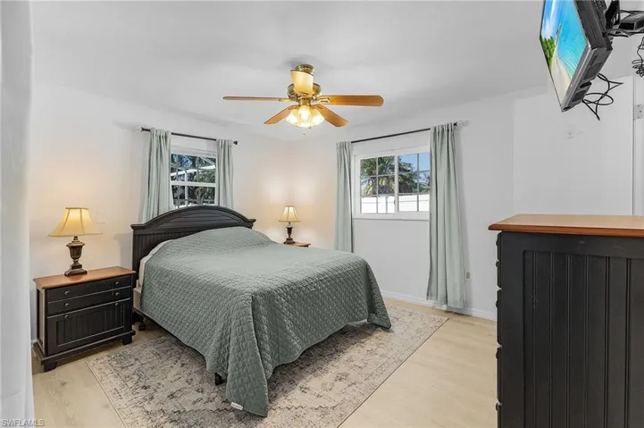 Bedroom with light wood-style flooring, windows that provide natural light, and a ceiling fan.