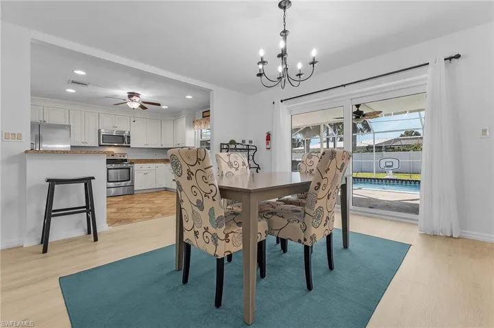 The dining area with beautiful light wood-type flooring and notable chandelier opens to the fenced backyard with an oversized pool cage, large swimming pool and above-ground spa.