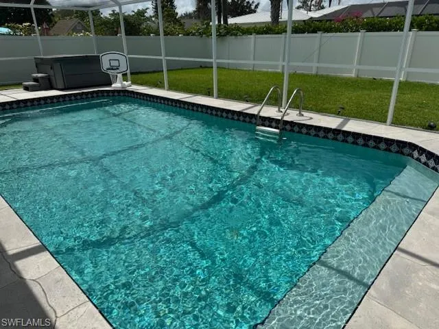 View of pool with an above-ground spa, the pool cage and a fenced backyard.