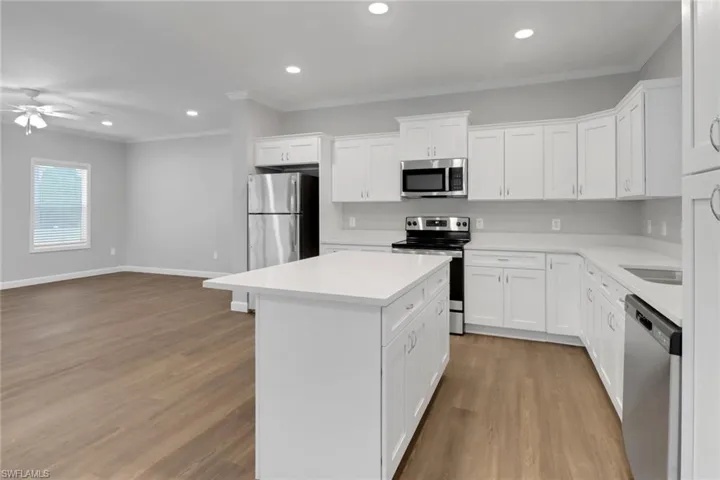 Kitchen with stainless steel appliances, laminated floors, an island, crown molding, and white cabinetry
