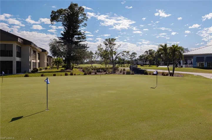Manicured putting green with multiple flagsticks, bordered by mature trees and residential buildings