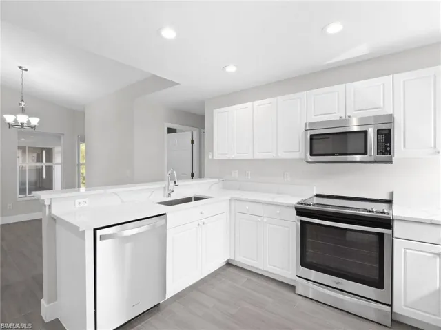Kitchen with stainless steel appliances, a peninsula, white cabinets, a chandelier, and light wood finished floors
