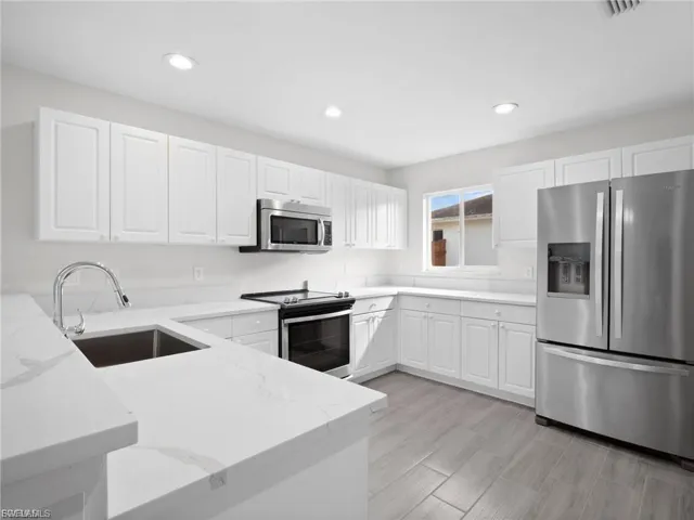 Kitchen with stainless steel appliances, white cabinetry, light stone countertops, recessed lighting, and light wood finished floors