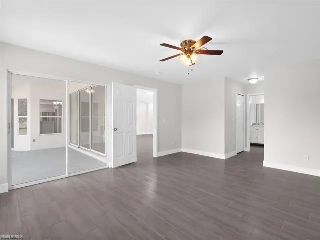 Unfurnished living room featuring ceiling fan and dark wood-style flooring
