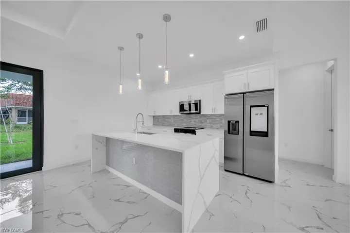 Contemporary kitchen featuring a waterfall island with a stainless steel sink, a matching backsplash, and pendant lighting