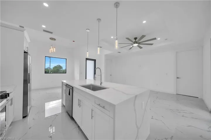 Open-concept kitchen featuring a waterfall island with a stainless steel sink, pendant lighting, and white cabinetry