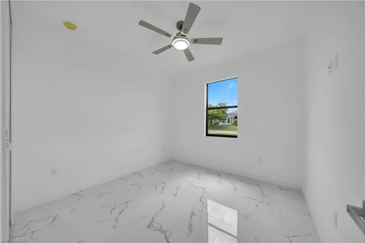 Bright room featuring large format marble-look tile flooring, a window with exterior views, and a ceiling fan with integrated lighting