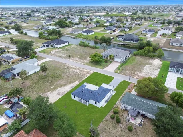 Newly constructed residence with a dark shingle roof and white exterior, featuring a paved driveway and a manicured lawn