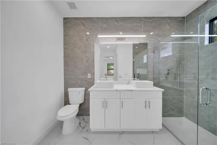 Contemporary bathroom featuring a dual vanity with vessel sinks, a glass-enclosed shower, a built-in shower bench, and large-format tile flooring