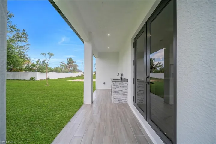 Covered patio featuring wood-finish tile flooring, recessed lighting, and an outdoor kitchen with a dark countertop and stone-tiled base