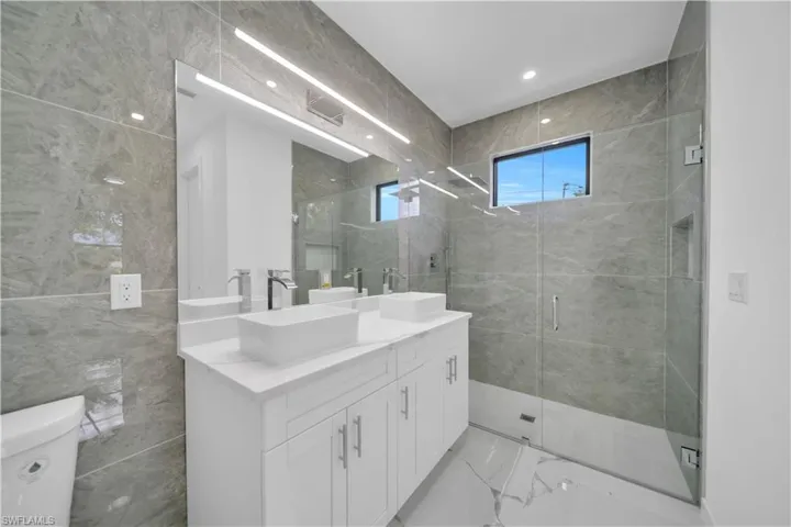 Contemporary bathroom featuring a double vanity with vessel sinks, white cabinetry, and a large frameless mirror