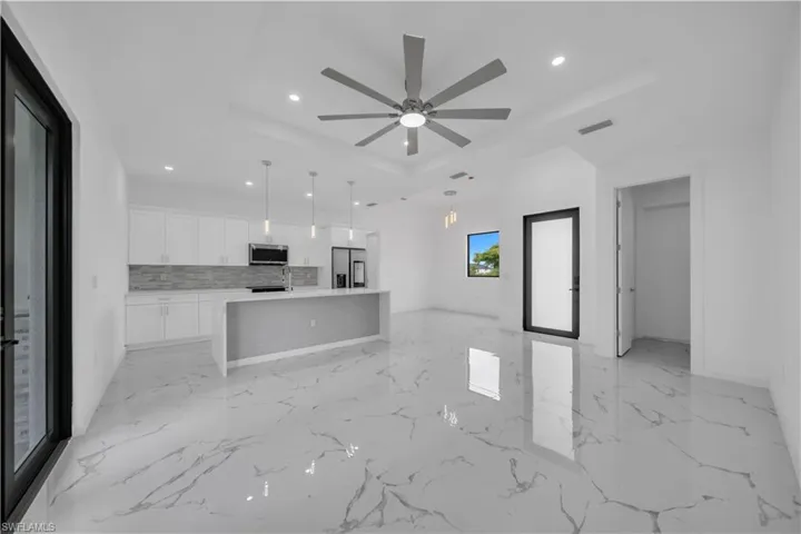 Open-concept living area featuring large format white tile flooring with grey veining, a contemporary ceiling fan, and recessed lighting