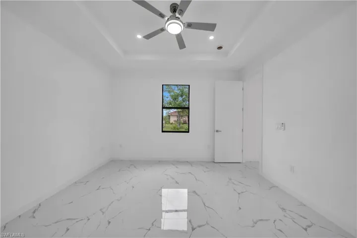Spacious room featuring white walls, large format tile flooring, a tray ceiling with a ceiling fan, recessed lighting, and a window with black trim