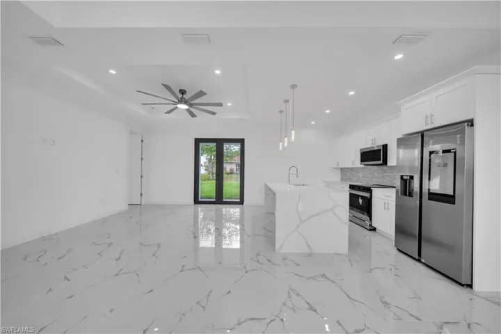 Open-concept living space with large-format tile flooring, a tray ceiling featuring recessed lighting and a ceiling fan, and black-framed French doors